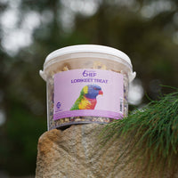 Container of Feather Chef Lorikeet Treats on a rock with blurred greenery in the background